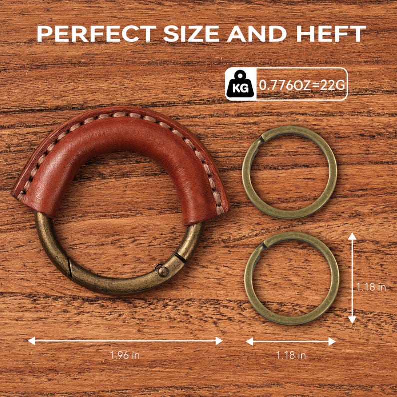 May include: A brown leather handle with a metal clasp and two metal rings. The handle is stitched with white thread. The text "PERFECT SIZE AND HEFT" is at the top. The rings are 1.18 inches in diameter. The handle is 1.96 inches long.