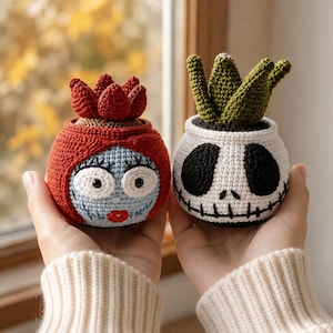 May include: Two crocheted plant pots featuring character faces. The left pot is light blue with red hair and a red succulent top. The right pot is white with black eye sockets, a stitched mouth, and a green succulent top. Both are round and textured.