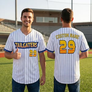 May include: White baseball jersey with vertical navy blue stripes, featuring the word "TAILGATERS" in blue and gold, and the number "29" in gold and orange. The jersey has blue trim and is worn by a person.