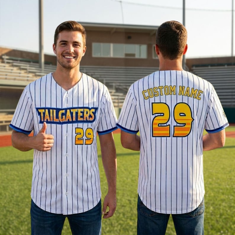 May include: White baseball jersey with vertical navy blue stripes, featuring the word "TAILGATERS" in blue and gold, and the number "29" in gold and orange. The jersey has blue trim and is worn by a person.
