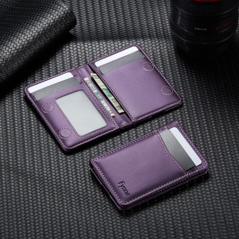 May include: Purple leather wallet, open to display cards and cash. A smaller, closed wallet is next to the open one. The wallets have white stitching and the brand name "Fynne" is visible on the closed wallet.