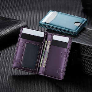 May include: Purple bi-fold wallet with multiple card slots and a clear ID window. The wallet is open, revealing several cards and cash. A teal cardholder is visible in the background. The wallets are made of leather and have a stitched design.
