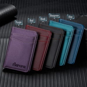 May include: A collection of leather cardholders in various colors: purple, red, black, bluegreen, and blue. Each cardholder has a pocket and is stitched around the edges. The word "Aurora" is embossed on the purple cardholder.