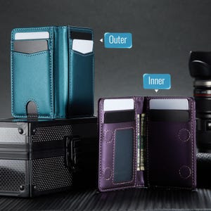 May include: Two leather card wallets, one teal and one purple, are displayed. The teal wallet is closed, while the purple wallet is open, revealing card slots and a cash compartment. The wallets are on a black surface.
