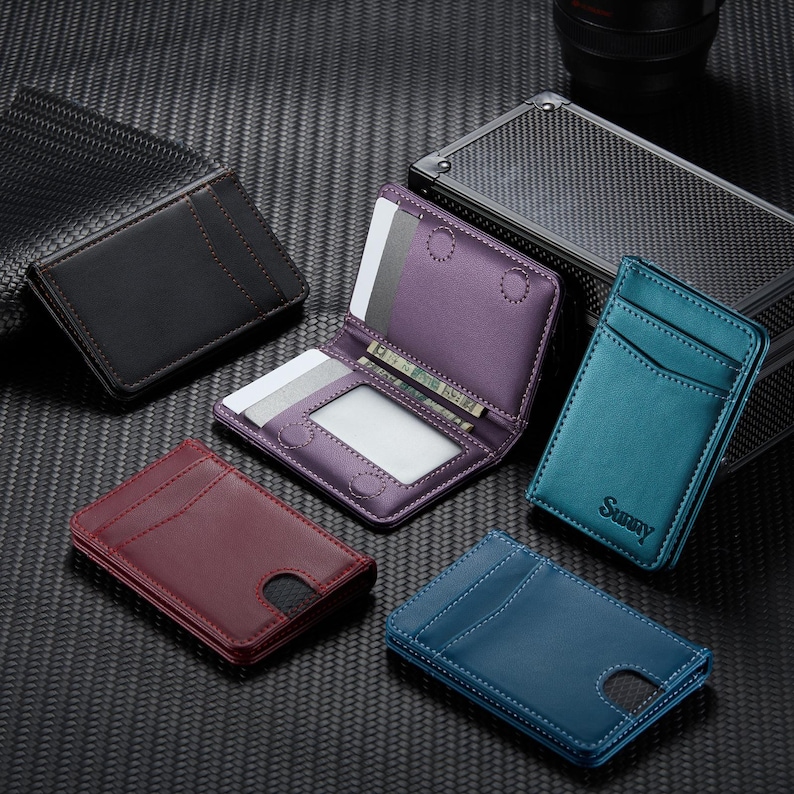 May include: A collection of leather cardholders in various colors, including black, burgundy, teal, and blue. One cardholder is open, revealing card slots and a clear ID window. The teal cardholder has the word "Sunny" embossed on it.