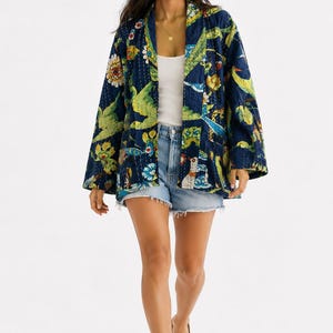 May include: A quilted jacket featuring a dark blue base with a vibrant, multicolored floral and bird print, a white tank top, light blue denim shorts with a frayed hem, and brown leather sandals with multiple straps and a toe loop design.