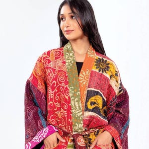 May include: A patchwork kimono robe in vibrant colors, including red, orange, and purple. The robe features a mix of floral and geometric patterns, with a matching belt and pockets. The sleeves are wide, and the robe appears to be made of a soft, quilted fabric.