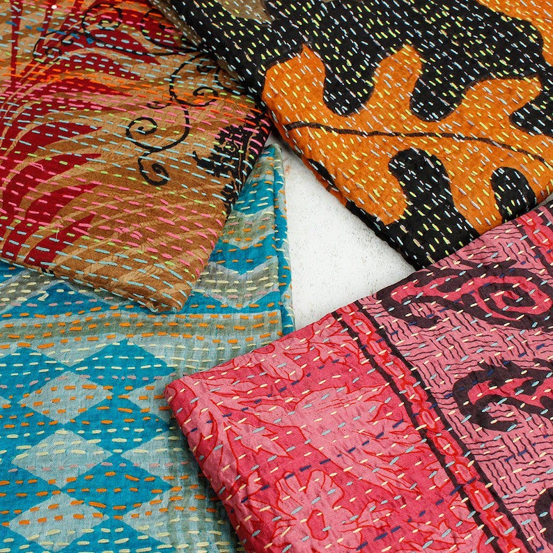 May include: A collection of colorful, patterned textiles. The fabrics feature intricate stitching and designs in shades of red, orange, blue, and black. The textiles appear to be folded or layered, showcasing the variety of patterns.