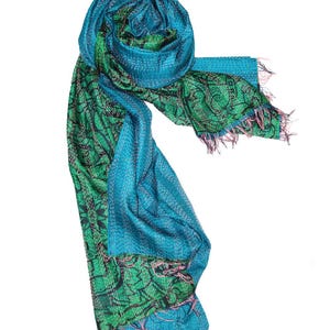 May include: A vibrant, handmade scarf in shades of teal and green. The scarf features intricate stitching and a detailed pattern, with a fringed edge. The design incorporates both solid and patterned sections, creating a visually appealing accessory.