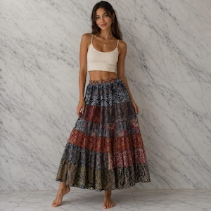 May include: A cream-colored cropped tank top with thin straps paired with a long, tiered maxi skirt featuring a multi-colored paisley and floral pattern in shades of blue, red, brown, and gold, with a gathered, flowing silhouette.