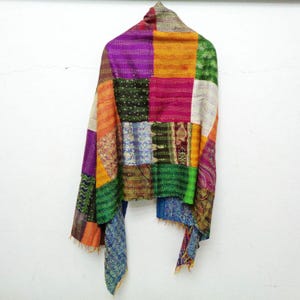 May include: A patchwork shawl with a variety of colorful fabric squares. The shawl features a mix of purple, orange, green, and blue hues. The garment is draped, showcasing its design and texture. The shawl is a unique, handcrafted accessory.