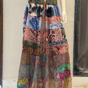 Può includere: Una gonna lunga a balze caratterizzata da un design patchwork con vari motivi multicolori, tra cui stampe paisley, floreali e geometriche. La gonna presenta una vita elasticizzata con un cordoncino centrale dotato di una nappa color ottanio.