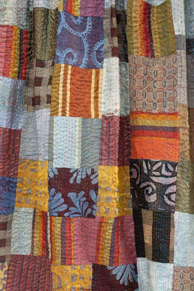 May include: A patchwork textile featuring a variety of fabrics in a range of colors including gold, orange, blue, and burgundy. The design incorporates geometric shapes and patterns, with visible stitching throughout. The textile appears to be a quilt or decorative fabric.