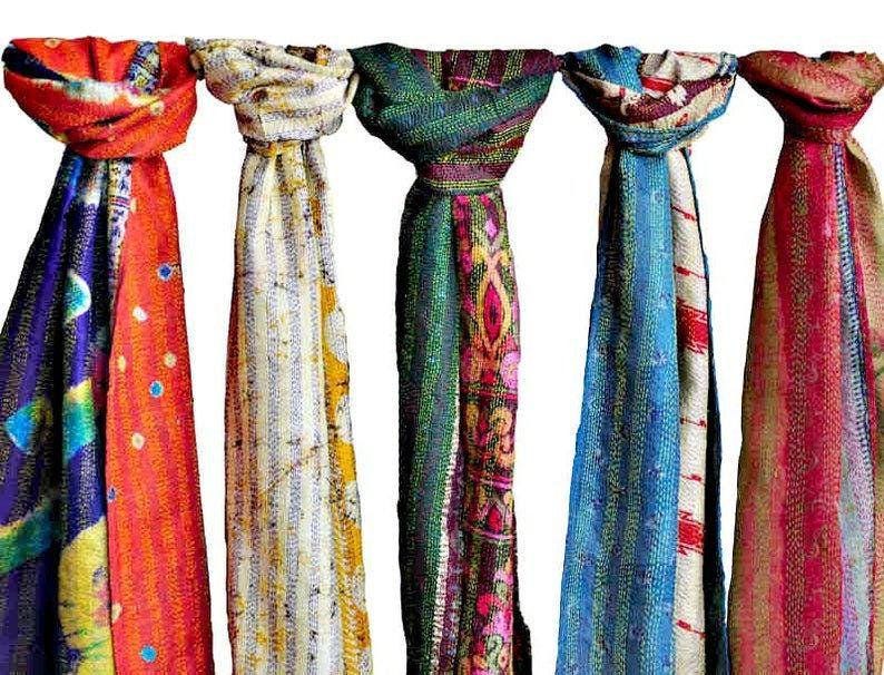 May include: Five colorful scarves hanging against a white background. The scarves display a variety of patterns and colors, including red, orange, blue, green, and yellow. Each scarf is unique, with different designs and textures.
