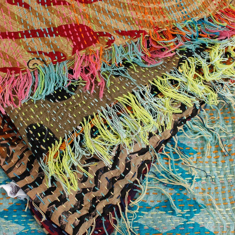 May include: A colorful, patchwork textile with a variety of patterns and textures. The piece features a mix of brown, red, and blue fabrics, accented with vibrant fringe in shades of pink, yellow, and turquoise. The stitching adds a handcrafted feel.