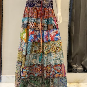 Könnte beinhalten: Ein bodenlanger Stufenrock mit einem dunkelblauen elastischen Bund und einem Kordelzug. Der Rock besteht aus mehreren horizontalen Bahnen mit einer Vielzahl bunter Muster, darunter Paisley-, Blumen- und geometrische Designs.