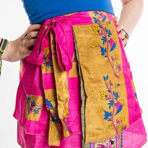 May include: A vibrant pink wrap skirt with gold and floral accents. The skirt features a wrap design with a tie closure. The skirt has a patchwork design with a variety of patterns and colors, including gold, pink, blue, and yellow.