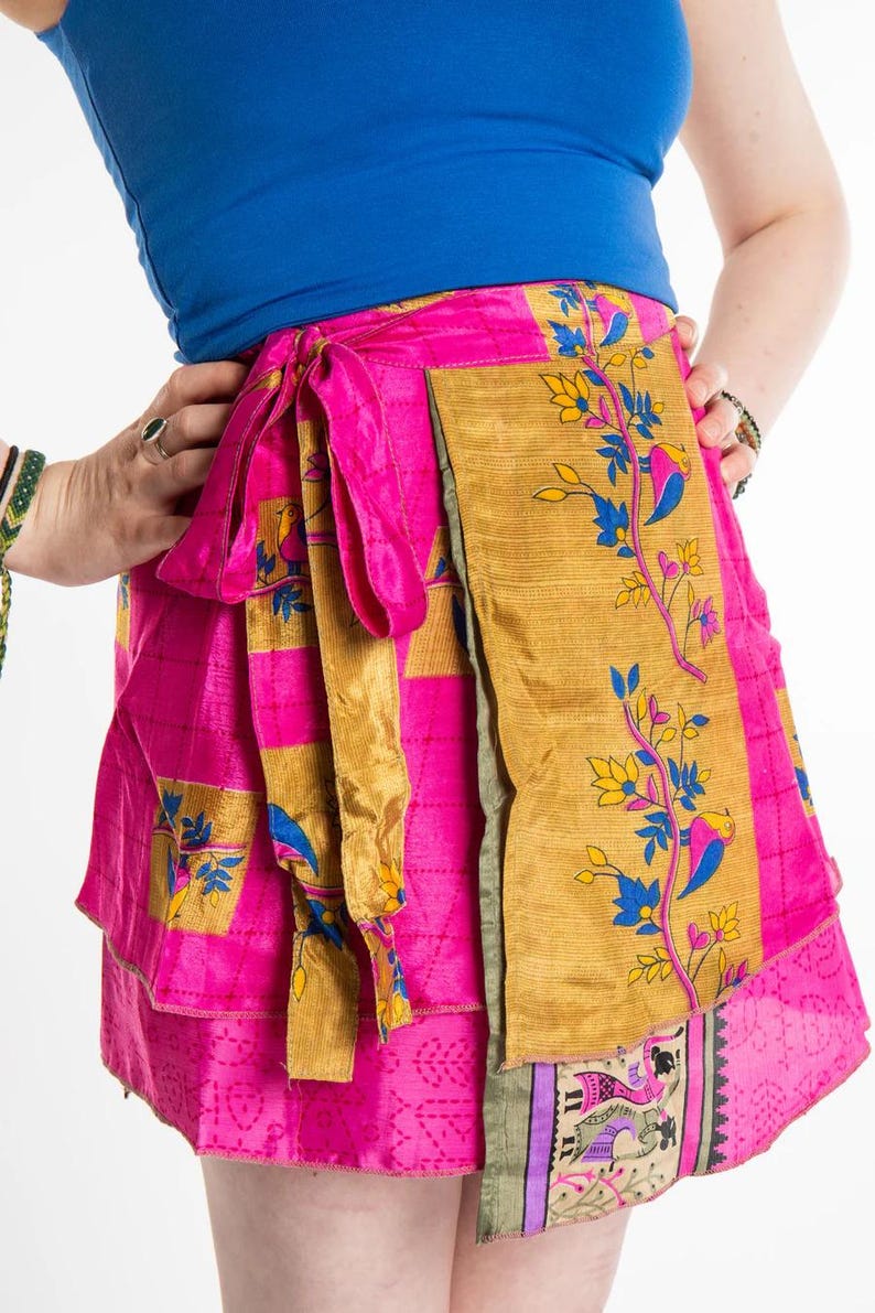 May include: A vibrant pink wrap skirt with gold and floral accents. The skirt features a wrap design with a tie closure. The skirt has a patchwork design with a variety of patterns and colors, including gold, pink, blue, and yellow.