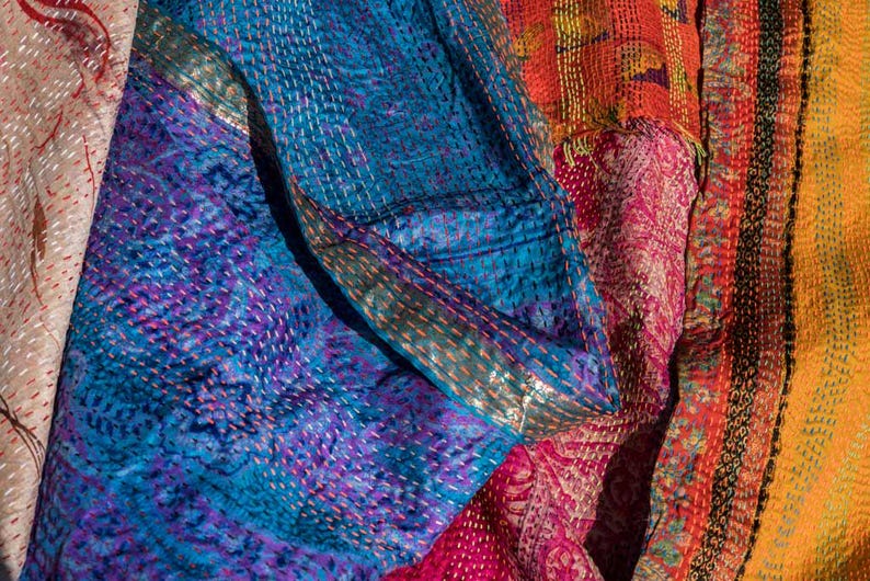 May include: Close-up of a patchwork textile with vibrant colors. The fabric features intricate stitching and a mix of blue, purple, pink, orange, and yellow hues. The design includes floral and geometric patterns, creating a textured and visually rich surface.