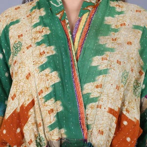 May include: A patchwork kimono-style robe in shades of green, cream, orange, and purple. The robe features a V-neck and is adorned with intricate stitching and a variety of patterned fabrics. The design includes geometric and floral motifs.
