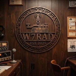 May include: A circular wooden wall sign featuring a radio tower and telegraph key icon with the text W7RAD EST. 2025, mounted on dark wood panelling in a room filled with vintage radio equipment, including multiple transceivers and a microphone.