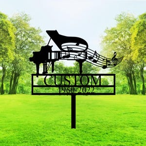 May include: Black metal garden stake with a grand piano silhouette and musical notes. The stake has the word "CUSTOM" and the years "1960-2022". The design is set against a green lawn and trees.