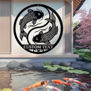May include: Black metal wall art depicting two koi carp in a circular design, with the text "CUSTOM TEXT" below. The artwork is set against a neutral background, with a pond and koi carp visible in the foreground.
