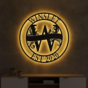 May include: A black metal sign with the name "WINSLET" in a circular design, featuring a large letter "W" in the center and the text "EST 2020". The sign is illuminated with a warm yellow glow.