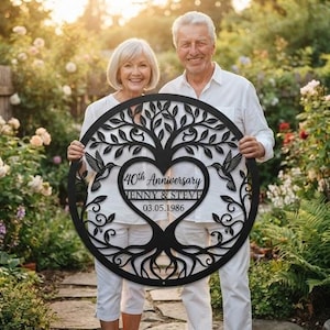 May include: A circular black metal wall art piece featuring a laser-cut tree of life design with two hummingbirds and a central heart shape. The text reads 40th Anniversary, Jenny & Steve, and 03.05.1986 in a decorative script and sans-serif font.