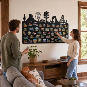 Könnte beinhalten: Eine große schwarze Metall-Wandtafel mit einer ausgeschnittenen Silhouette amerikanischer Wahrzeichen, darunter ein Route-66-Schild, ein Kaktus und die Golden Gate Bridge, bedeckt mit zahlreichen bunten Souvenir-Magneten aus verschiedenen Orten.