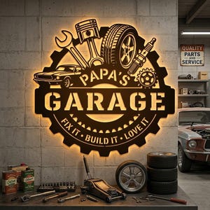 May include: A dark brown metal wall sign shaped like a gear with backlighting. It features a car, piston, tire, and spark plug graphic with the text "PAPA'S GARAGE" and "FIX IT • BUILD IT • LOVE IT" cut out from the center of the gear design.