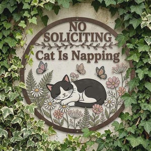 May include: A round metal sign with the text "NO SOLICITING Cat Is Napping." The sign features a sleeping black and white cat surrounded by flowers and butterflies. The sign is framed by a brown border and green ivy.