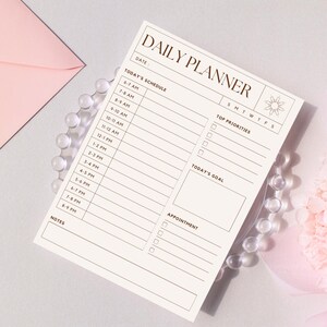 May include: A beige daily planner with the words "DAILY PLANNER" at the top. The planner includes sections for the date, schedule, top priorities, today's goal, and appointments. The planner is on a clear beaded plate.
