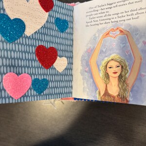 Pu&ograve; includere: Libro aperto con una pagina con sfondo blu con ovali bianchi e varie decorazioni a forma di cuore in rosso, blu, rosa e bianco. La pagina opposta presenta un'illustrazione di una donna che forma un cuore con le braccia.