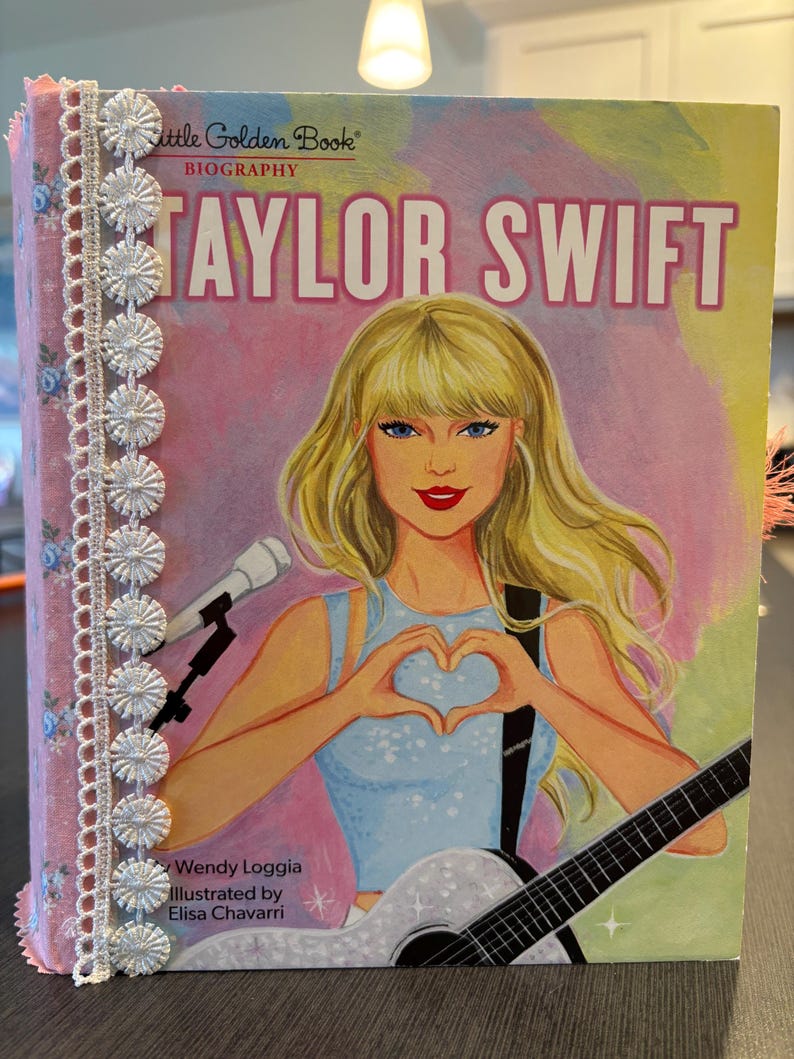 Pu&ograve; includere: Una biografia di Taylor Swift, un libro della collana Little Golden Book. La copertina presenta un'illustrazione di Taylor Swift con i capelli biondi, che forma un cuore con le mani. Il libro &egrave; decorato con tessuto floreale rosa e bordi in pizzo bianco.