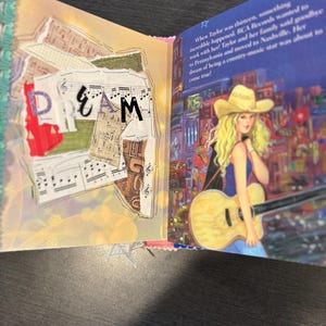Pu&ograve; includere: Libro aperto con la parola "DREAM" in lettere colorate. La pagina sinistra presenta note musicali e carta strappata. La pagina destra mostra un'illustrazione di una donna bionda con una chitarra, con un cappello da cowboy, con testo su una star della musica country.