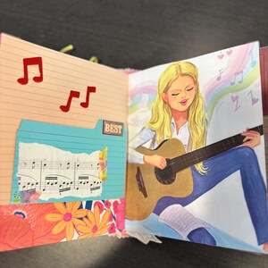 Pu&ograve; includere: Una pagina di diario con un disegno di una persona che suona la chitarra. L'illustrazione mostra una persona bionda con una camicia bianca e jeans blu. Il diario include note musicali e la parola "BEST".