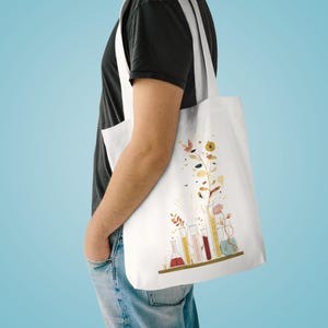May include: White tote bag with a botanical illustration. The design features colourful flowers and laboratory glassware, including test tubes and flasks. The artistic design has a floral theme, perfect for carrying essentials.