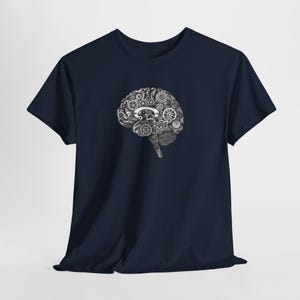 May include: Navy blue t-shirt featuring a detailed grayscale illustration of a brain composed of gears and mechanical components. The design is centered on the front of the shirt, offering a unique and intellectual aesthetic. The shirt is made of a soft material.