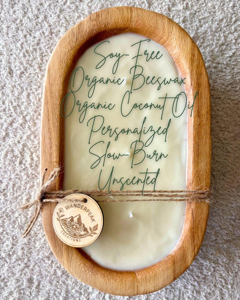 May include: A wooden candle holder with a cream-coloured candle. The candle is labelled "Soy-Free Organic Beeswax Organic Coconut Oil Personalized Slow-Burn Unscented." A small wooden tag with the Wanderpeak Creations logo is attached.