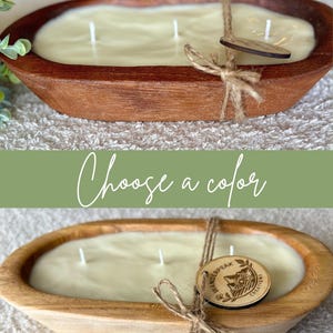 May include: A cream-coloured candle in an oval wooden bowl, with three wicks. A wooden tag is tied to the bowl with twine. The text "Choose a colour" is above the candle. The bowl is approximately 30 cm long.