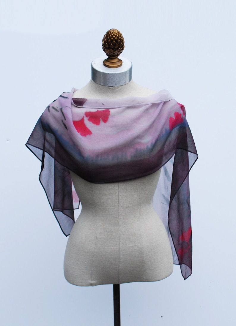 May include: A sheer scarf with a pink and purple ombre design and red floral accents. The scarf is draped over a mannequin.