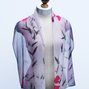May include: A sheer scarf with a floral print in shades of pink, red, and black. The scarf features a delicate floral pattern with black bamboo branches.