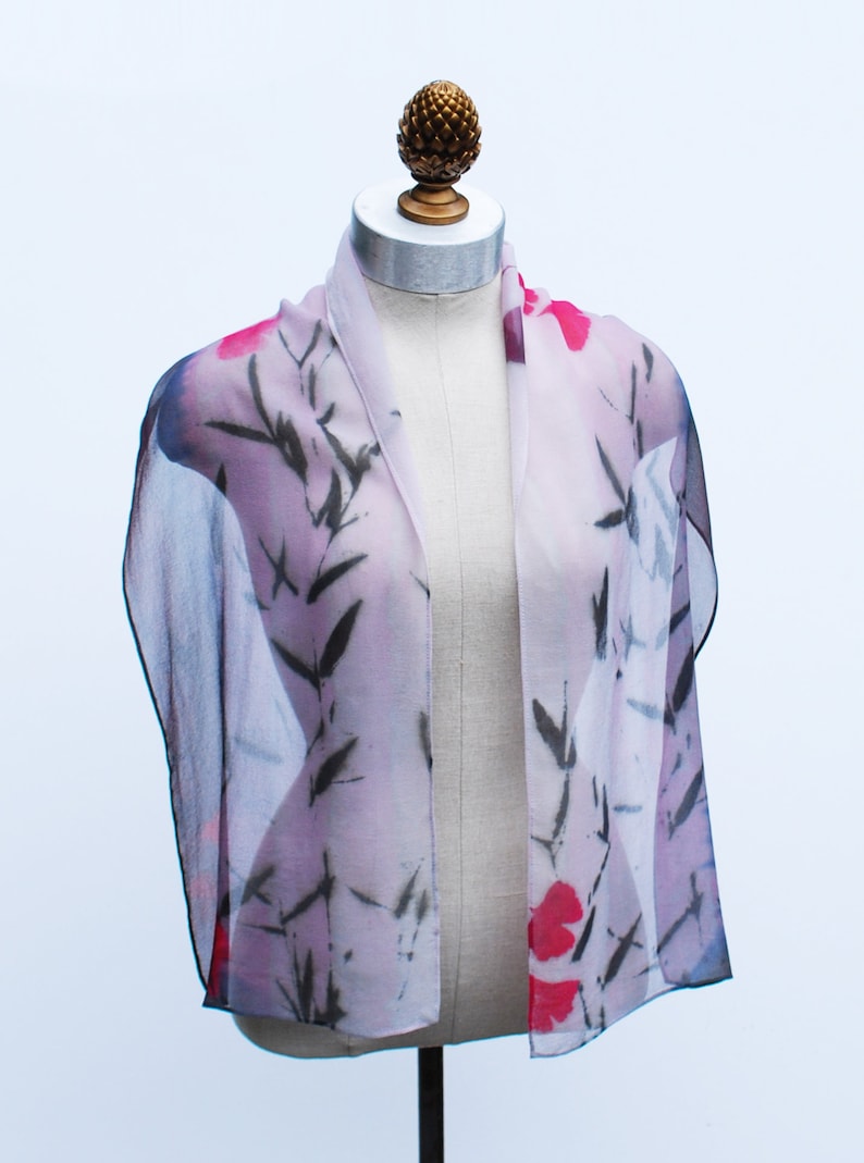 May include: A sheer scarf with a floral print in shades of pink, red, and black. The scarf features a delicate floral pattern with black bamboo branches.