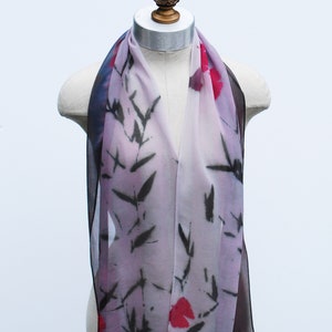 May include: A sheer scarf with a floral and leaf pattern in shades of pink, red, black, and white. The scarf is draped over a mannequin.