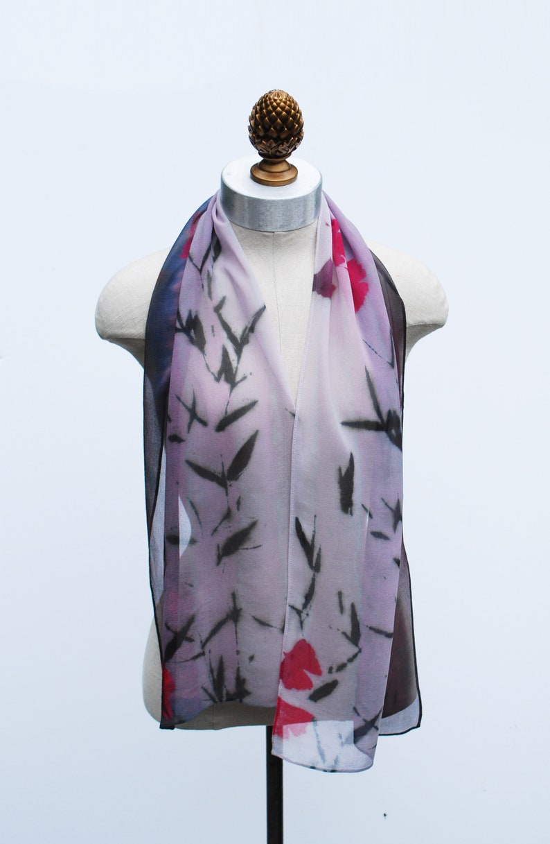 May include: A sheer scarf with a floral and leaf pattern in shades of pink, red, black, and white. The scarf is draped over a mannequin.
