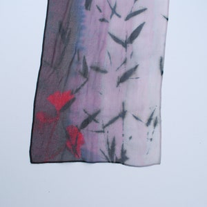 May include: A silk scarf with a black and red floral pattern on a purple background. The scarf has a frayed edge.