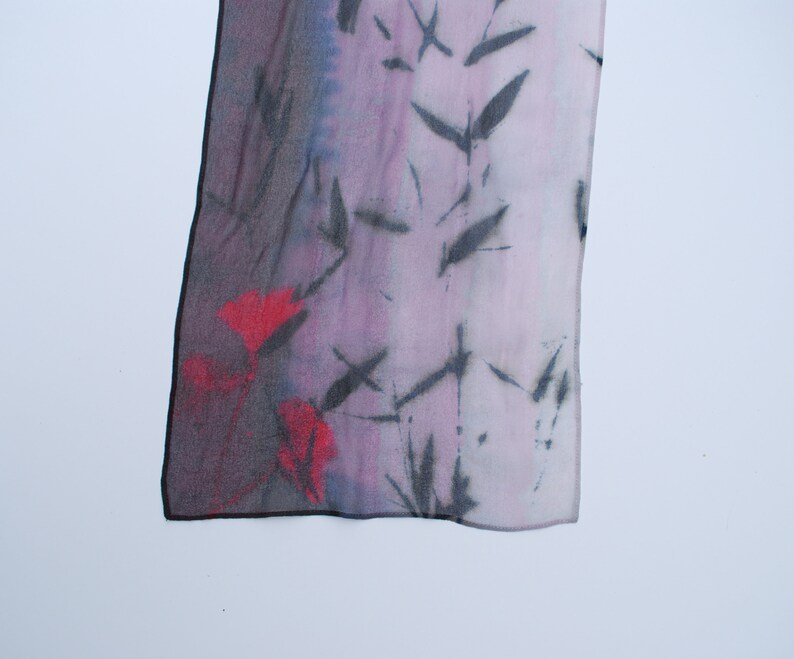 May include: A silk scarf with a black and red floral pattern on a purple background. The scarf has a frayed edge.