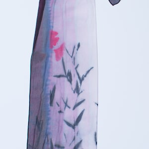 May include: A long, rectangular silk scarf with a pink and purple gradient background. The scarf features a black and white floral design and red floral accents.
