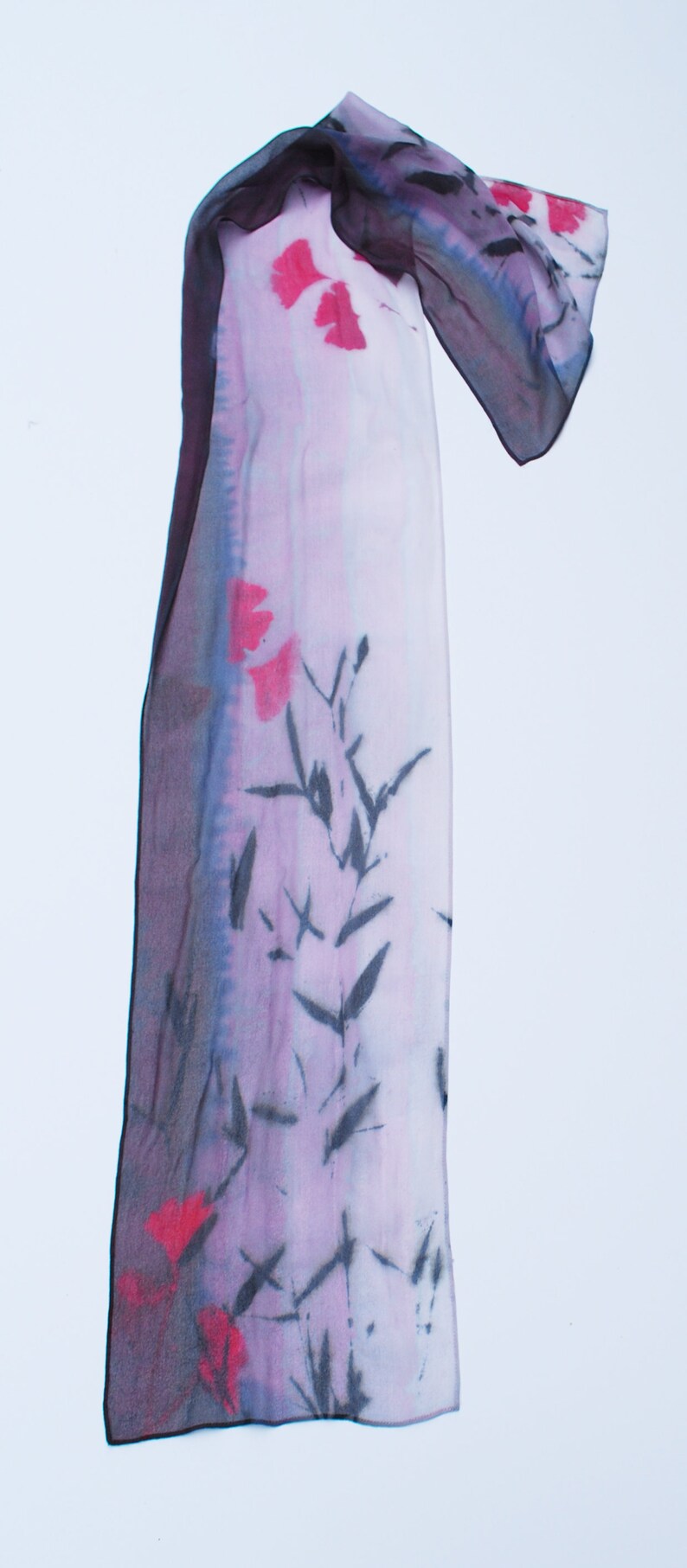 May include: A long, rectangular silk scarf with a pink and purple gradient background. The scarf features a black and white floral design and red floral accents.